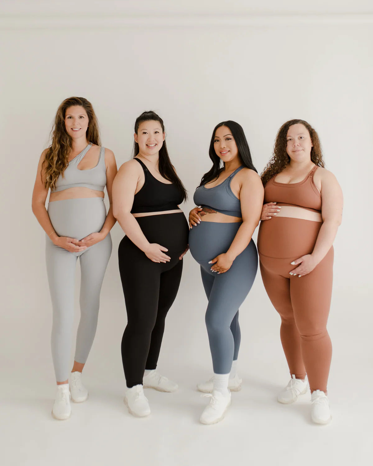 Four pregnant women wearing AXK maternity and nursing sports bras, leggings, and maternity activewear sets in gray, black, blue, and brown.