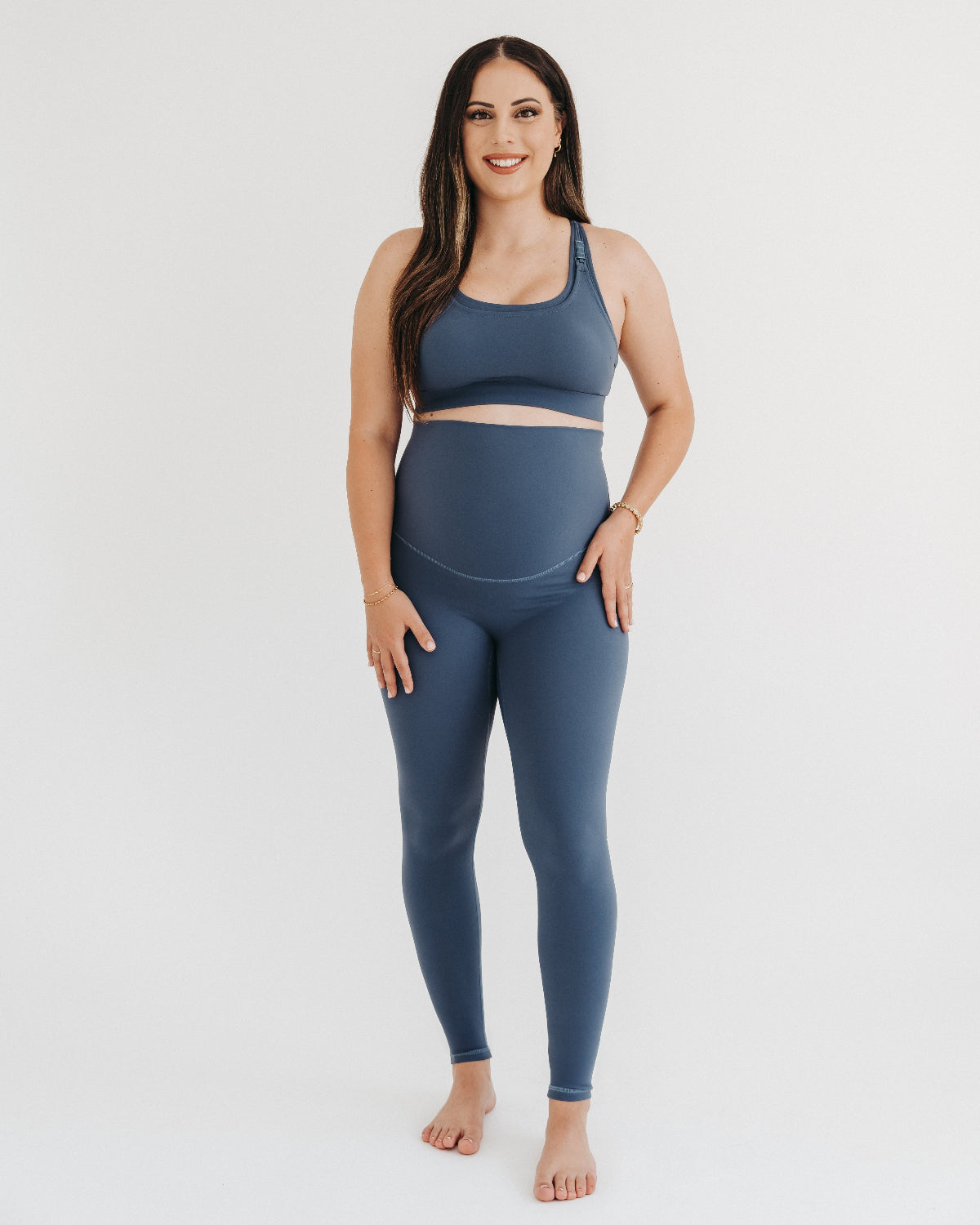 Pregnant woman wearing our best reviewed premium blue maternity leggings for 2026 with a flattering scrunch butt and matching trendy one shoulder nursing sports bra. Perfect for running, pregnancy yoga, lounge wear, and walking or hiking. Premium maternity athletic and activewear by AXK available in regular and plus sizes, petite and tall friendly.