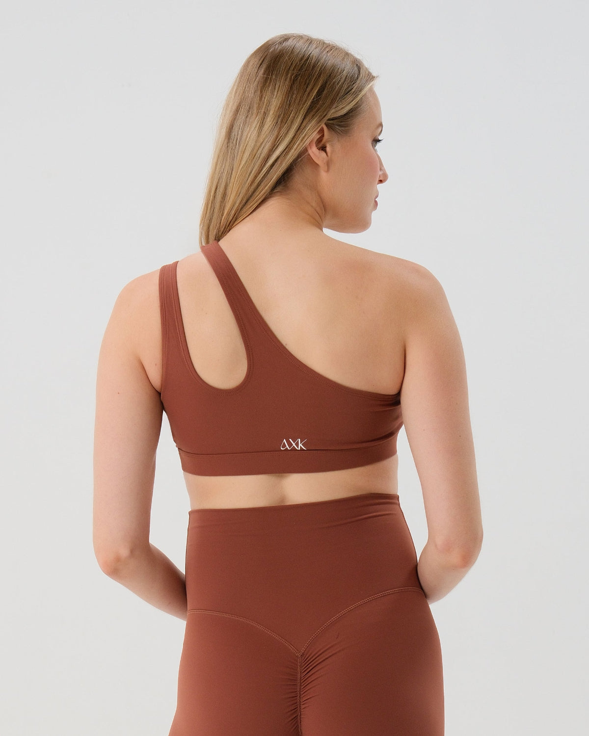 Back view of one-shoulder maternity and nursing sports bra and matching leggings. The bra features one-handed clip access for easy breastfeeding. Premium maternity activewear by AXK is offered in petite and plus size.