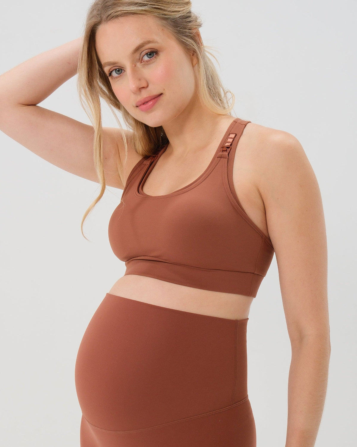 Pregnant woman wearing premium brown maternity bike shorts with a supportive high waist and matching high-impact, racerback maternity and nursing sports bra, standing against a white background. Premium maternity athletic and activewear by AXK - high quality petite, tall, and plus size maternity.