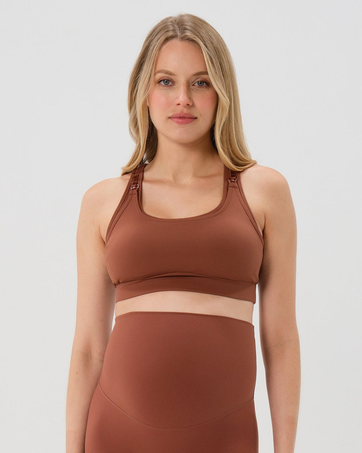 Pregnant woman wearing premium brown maternity bike shorts with a supportive high waist and matching high-impact, racerback maternity and nursing sports bra, standing against a white background. Premium maternity athletic and activewear by AXK - high quality petite, tall, and plus size maternity.