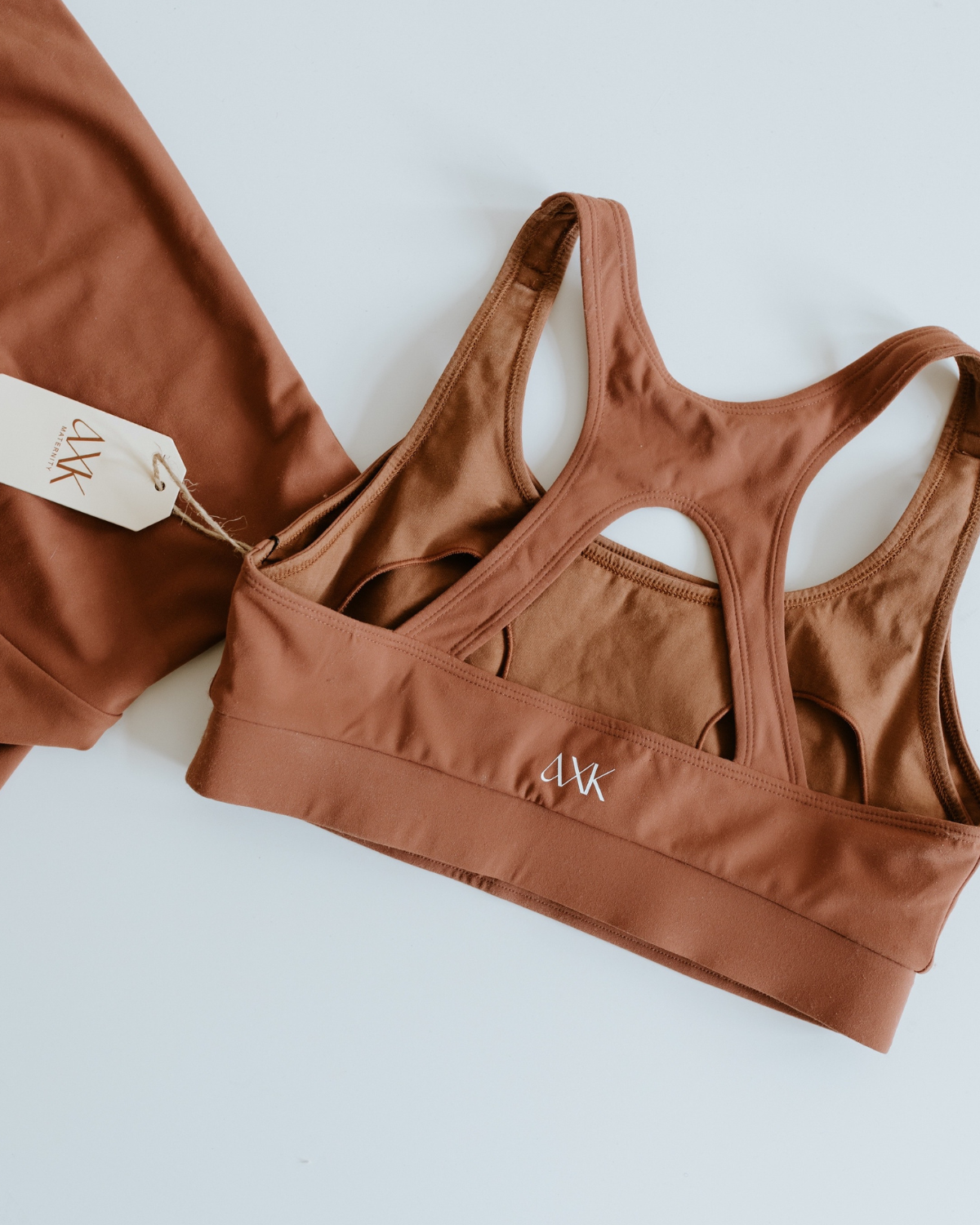Flat lay of a brown high-impact, racerback maternity and nursing bra, displayed on a white background with matching leggings partially visible. Premium maternity athletic and activewear by AXK.