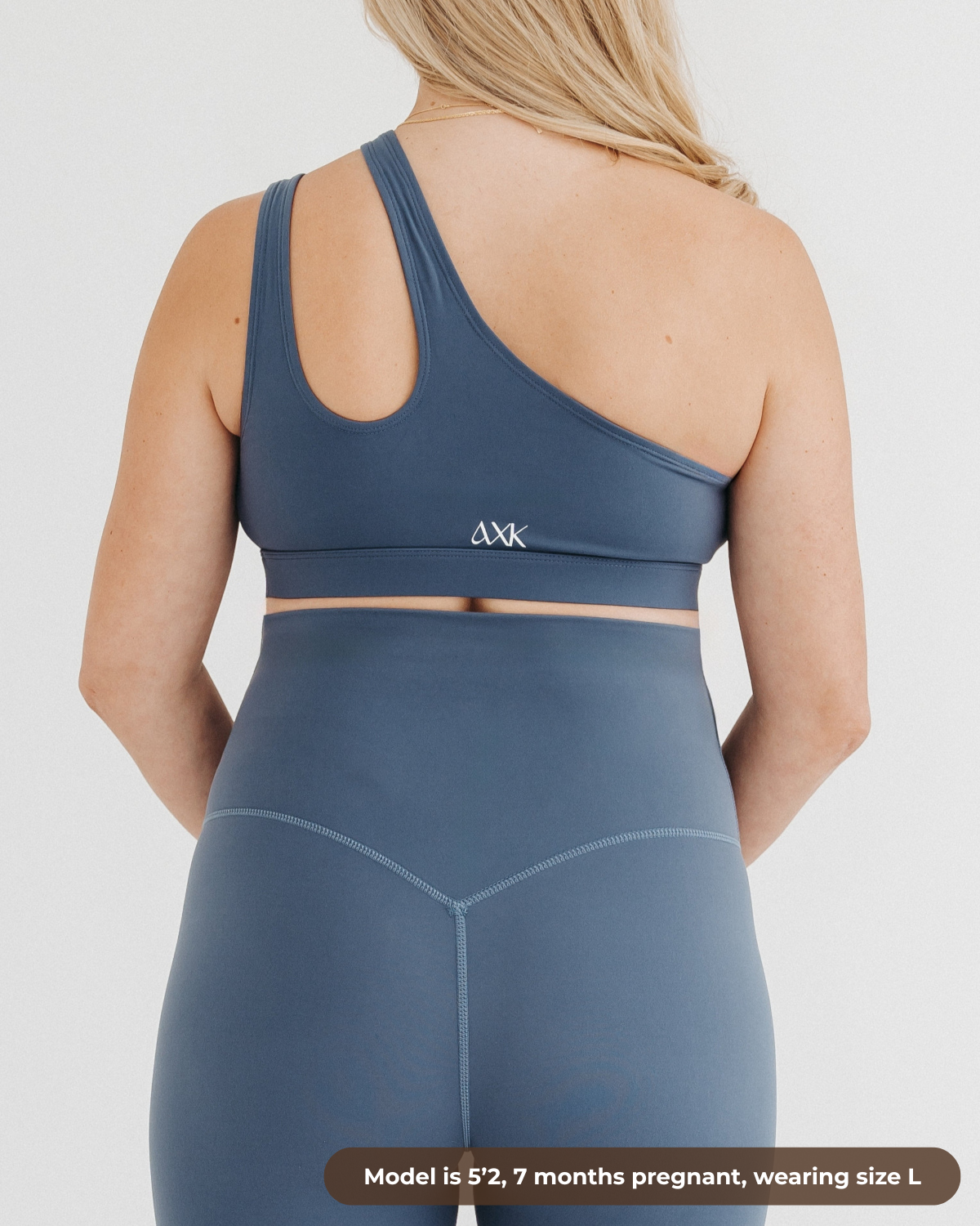Pregnant woman wearing a premium blue one-shoulder maternity and nursing sports bra. High quality 2026 maternity athletic and activewear by AXK in plus size, tall friendly, and petite friendly options. Best reviewed maternity fashion.