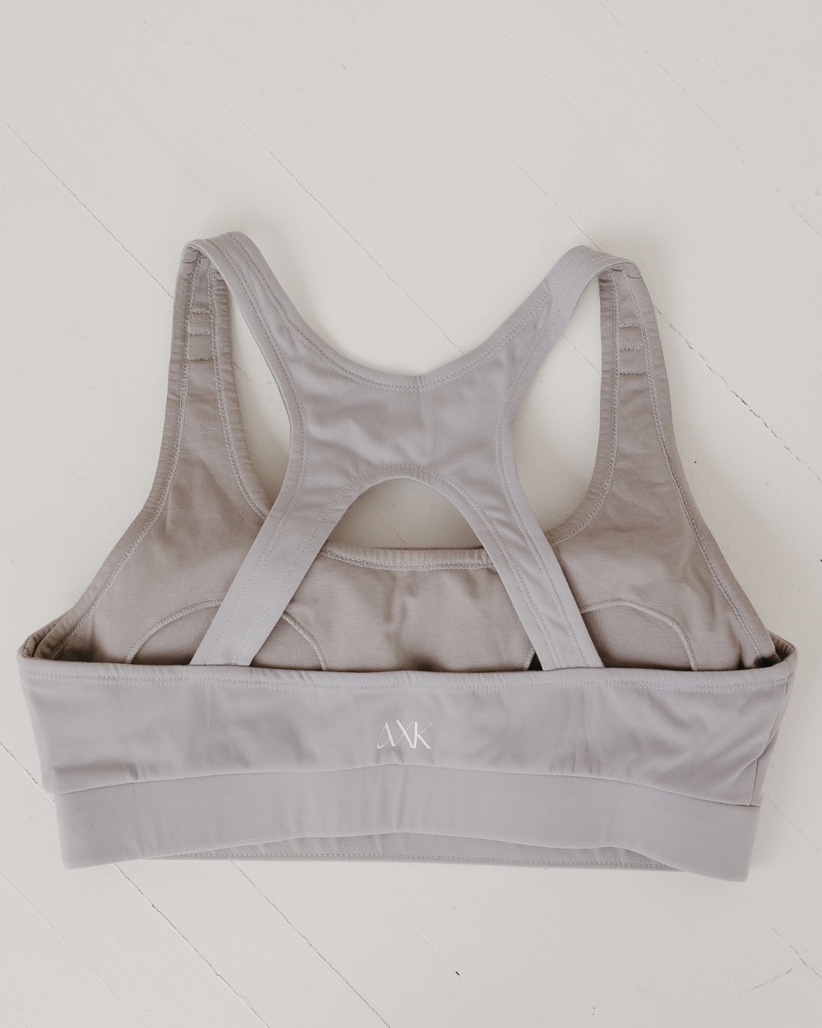 Flat lay of light-gray, high-impact, racerback nursing sports bra with clip-down straps and a smooth, seamless design, displayed on a white background. Premium maternity athletic and activewear by AXK.