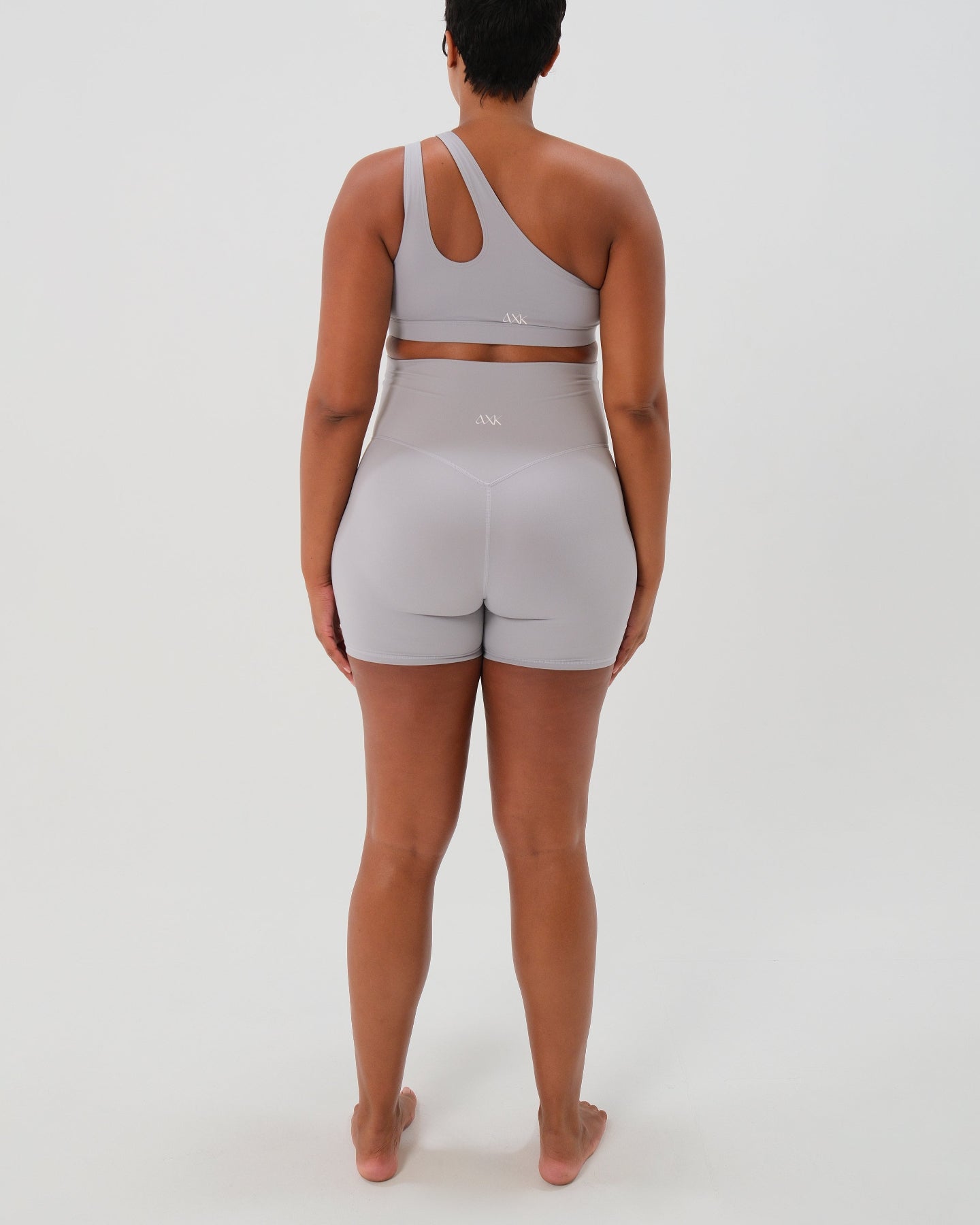 Pregnant plus size woman wearing premium light grey maternity bike shorts with a supportive high waist and matching high-impact, racerback maternity and nursing sports bra. Best reviewed premium maternity athletic and activewear by AXK, petite and tall friendly, in regular and plus size options.