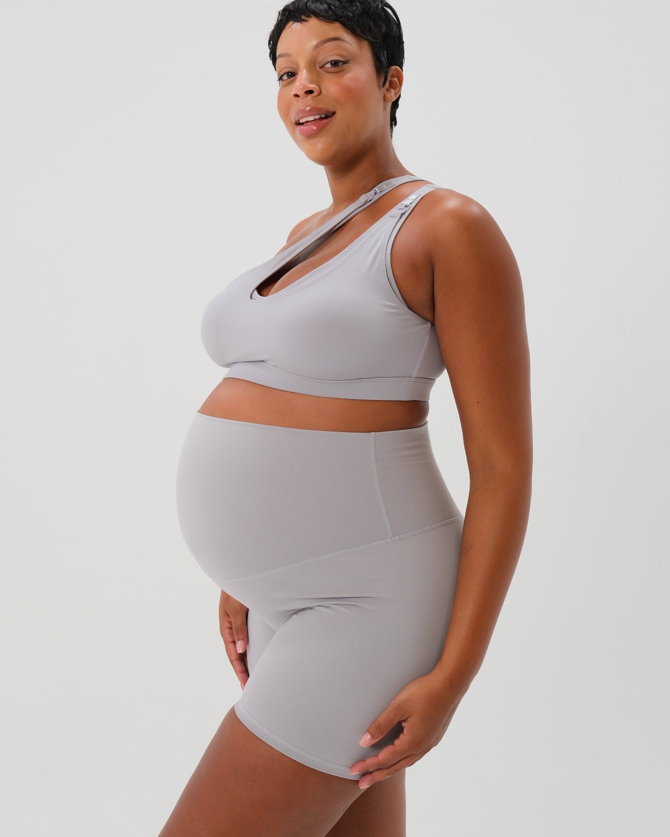 Pregnant plus size woman wearing premium light grey maternity bike shorts with a supportive high waist and matching high-impact, racerback maternity and nursing sports bra. Best reviewed premium maternity athletic and activewear by AXK, petite and tall friendly, in regular and plus size options.