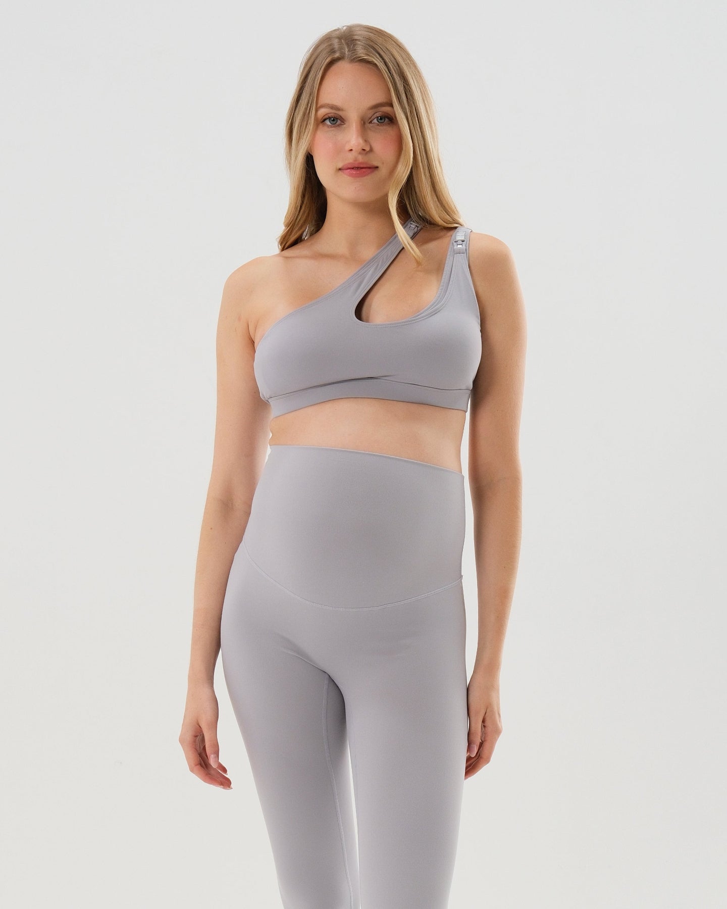 Light gray AXK one-shoulder maternity and nursing sports bra and matching leggings. The bra features one-handed clip access for easy breastfeeding. Our best reviewed 2026 premium maternity activewear by AXK is offered in petite and plus size.