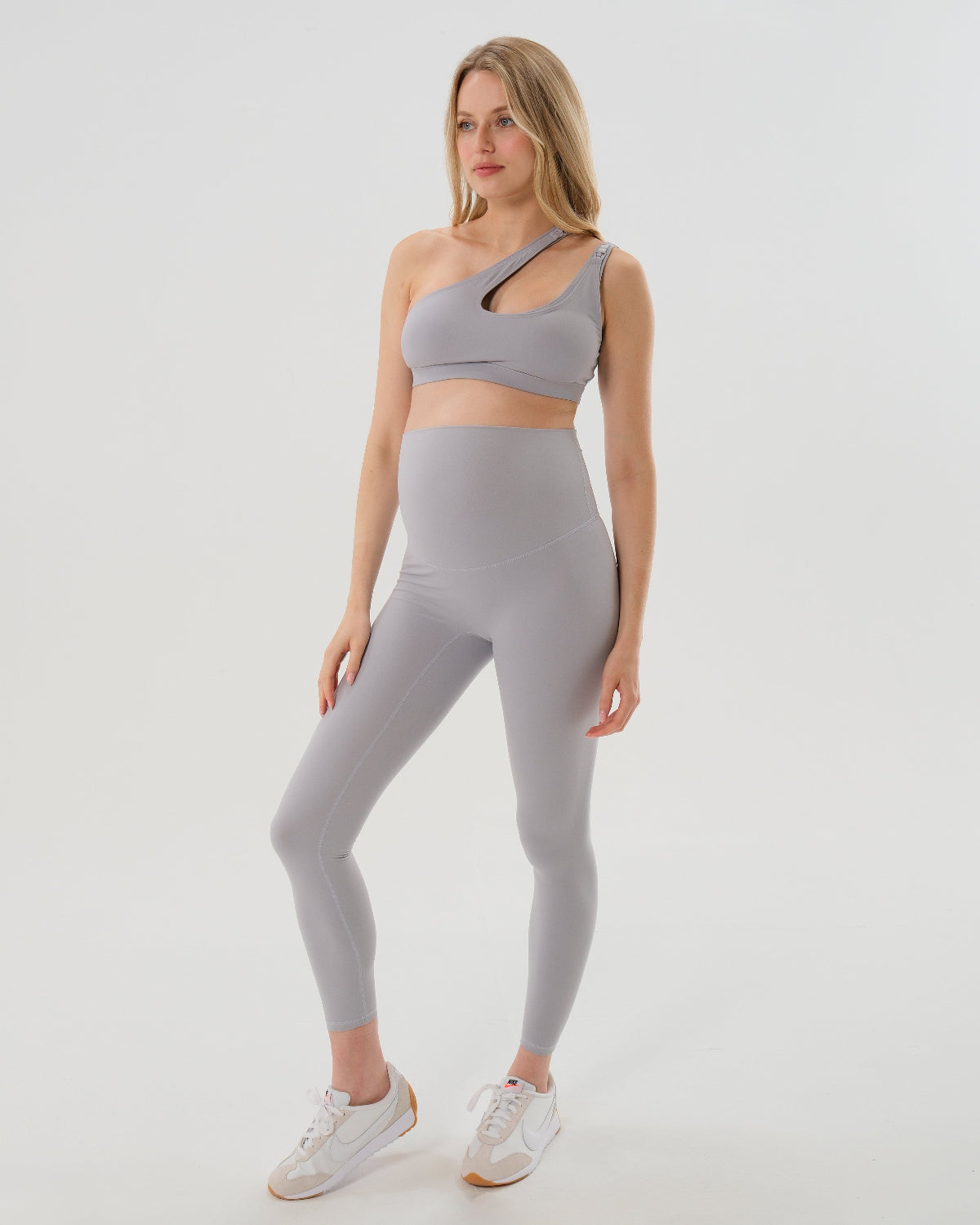 Pregnant woman wearing our best reviewed premium brown maternity leggings for 2026 with a flattering scrunch butt and matching trendy one shoulder nursing sports bra, standing against a white background. Premium maternity athletic and activewear by AXK.