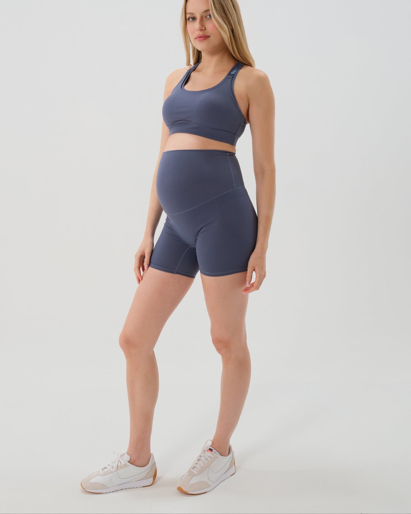 Pregnant woman wearing premium blue maternity bike shorts with a supportive high waist and matching high-impact, racerback maternity and nursing sports bra. Best reviewed 2026 premium maternity athletic and activewear by AXK, petite and tall friendly, in regular and plus size options. 