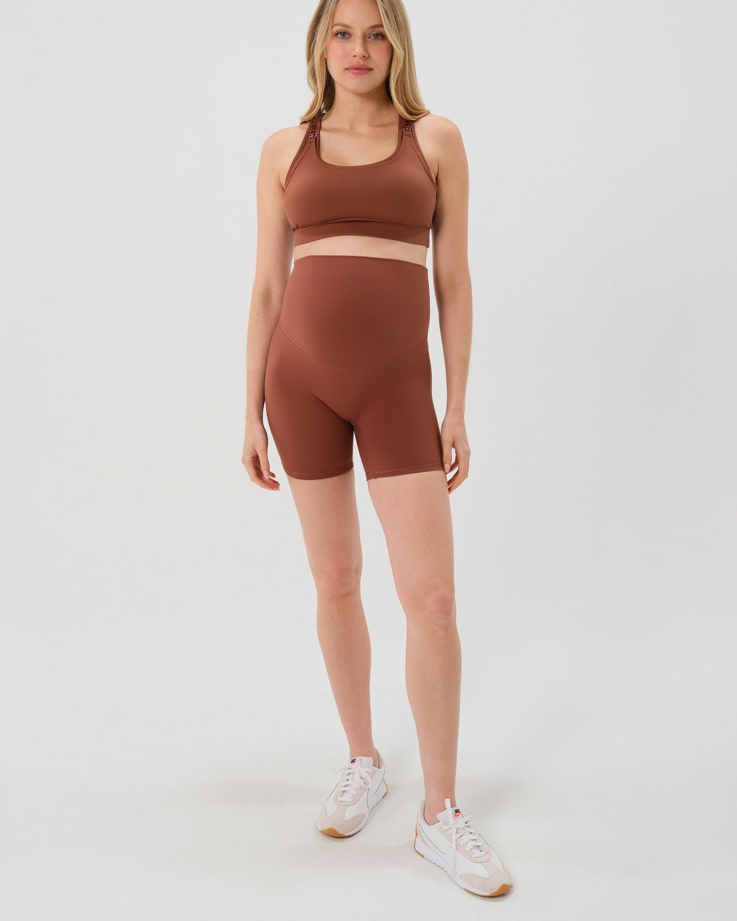 Pregnant woman wearing premium brown maternity bike shorts with a supportive high waist and matching high-impact, racerback maternity and nursing sports bra. Best reviewed 2026 premium maternity athletic and activewear by AXK, petite and tall friendly, in regular and plus size options. 