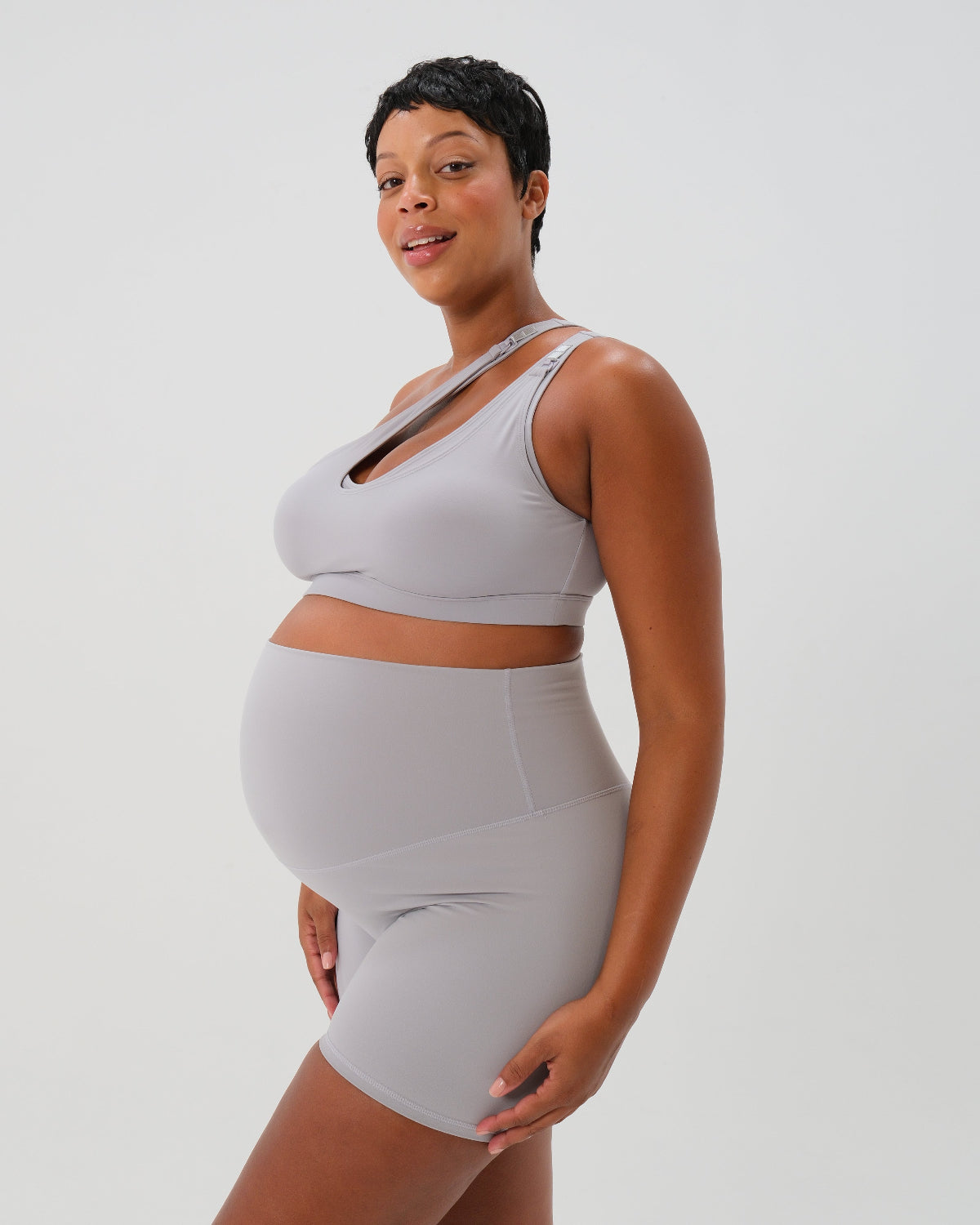 Light gray one-shoulder maternity and nursing sports bra and matching leggings. The bra features one-handed clip access for easy breastfeeding. Premium maternity activewear by AXK is offered in petite and plus size. 