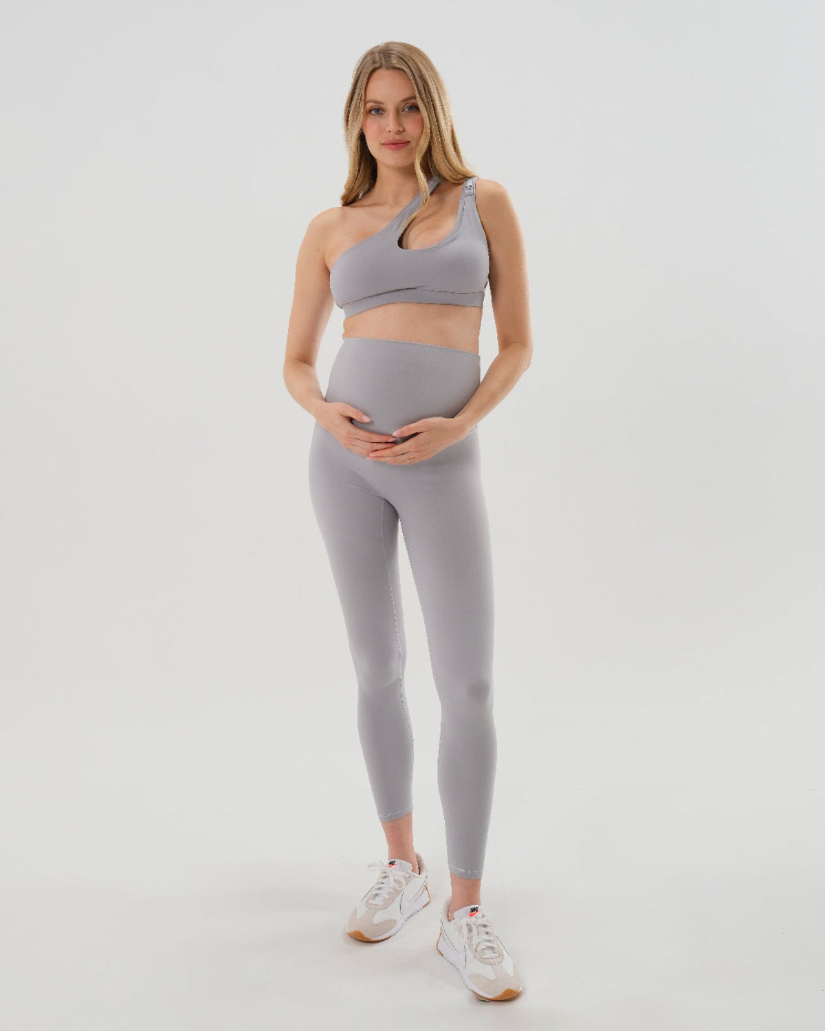 Pregnant woman wearing our best reviewed premium gray maternity leggings for 2026 with a matching trendy one shoulder nursing sports bra. Premium maternity athletic and activewear by AXK, available in plus sizes. Petite and tall friendly. 