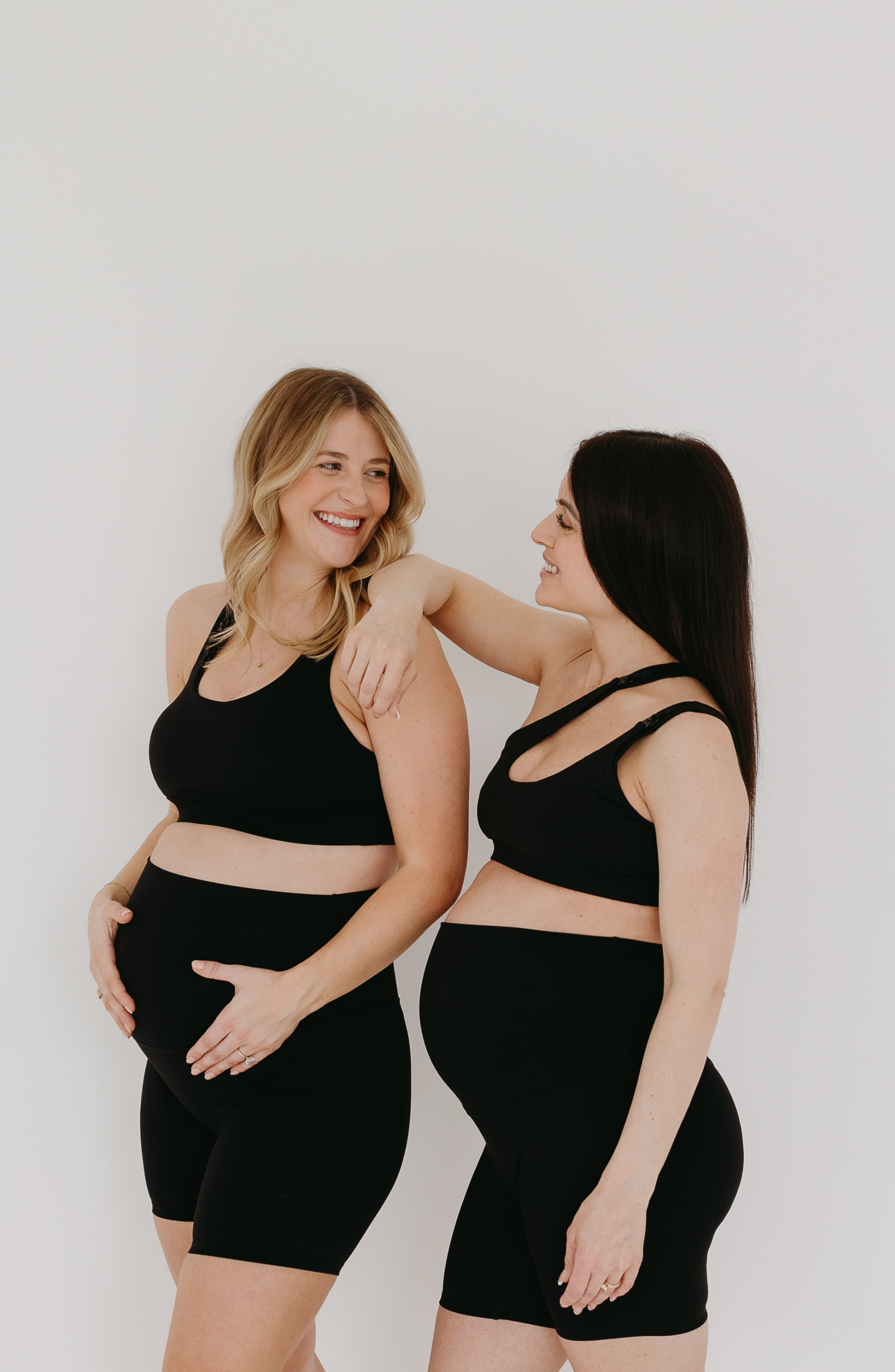 Two women wearing black maternity outfits against a white background